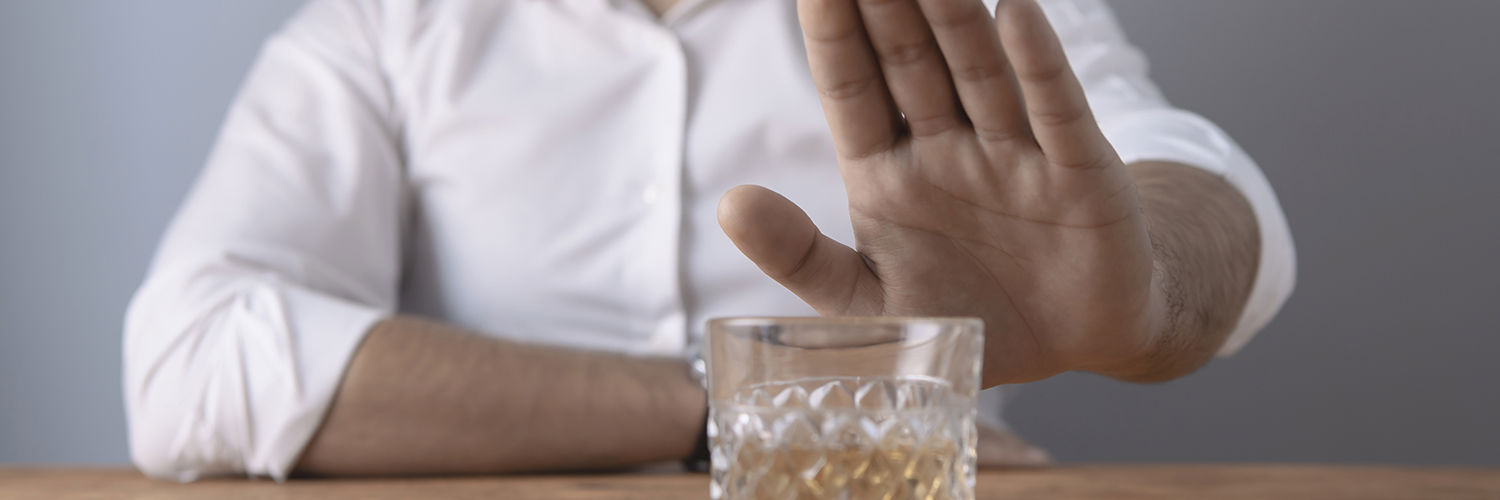 Mand der signalerer med hånden at han afviser et glas whisky