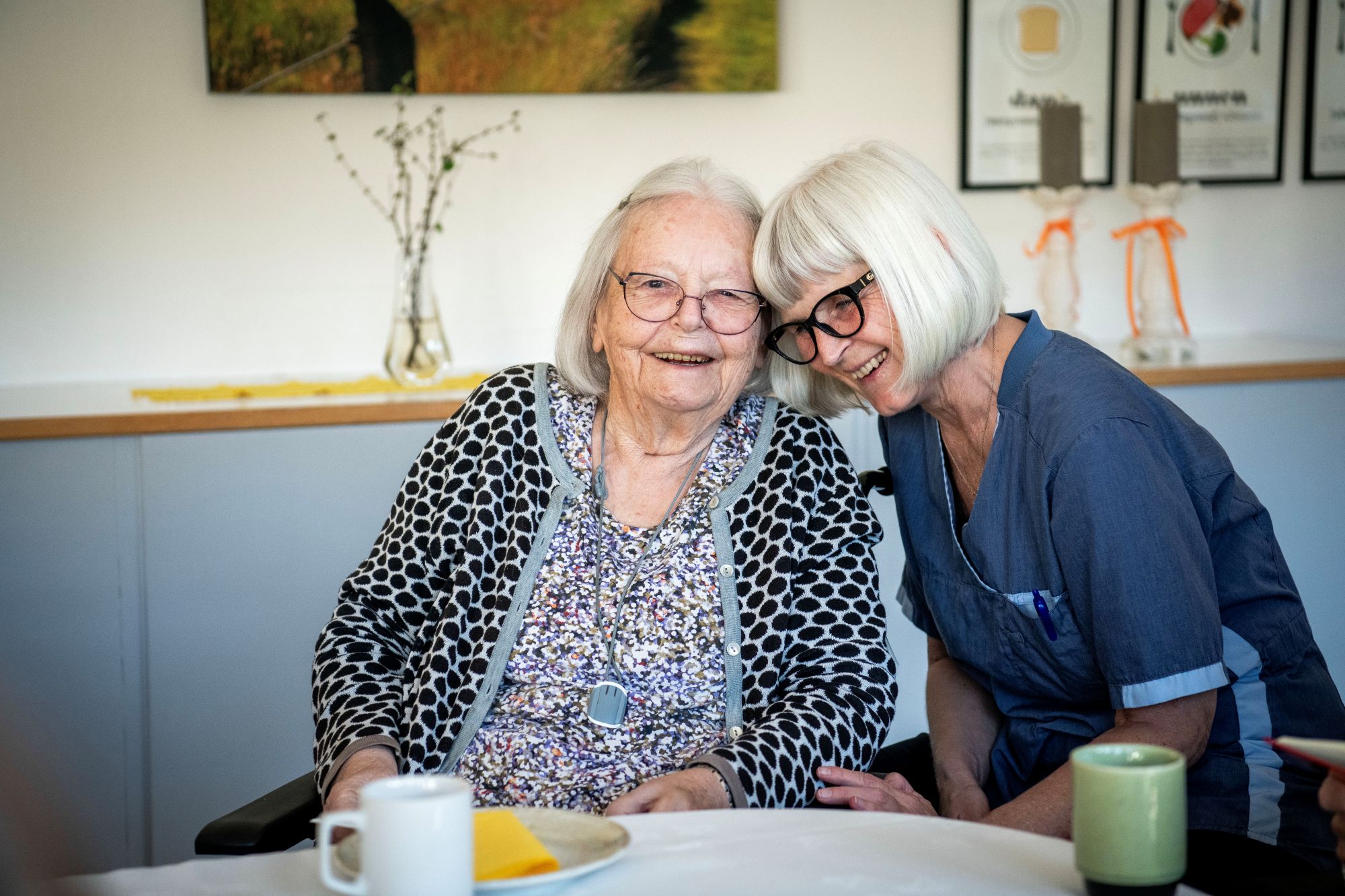 To damer, en borger og en plejepersonale, sidder med hovederne sammen og smiler