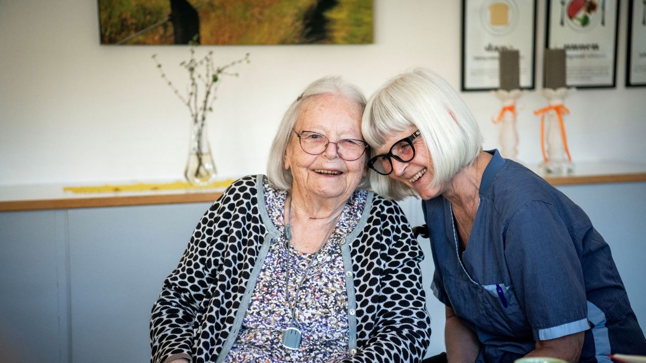 To damer, en borger og en plejepersonale, sidder med hovederne sammen og smiler