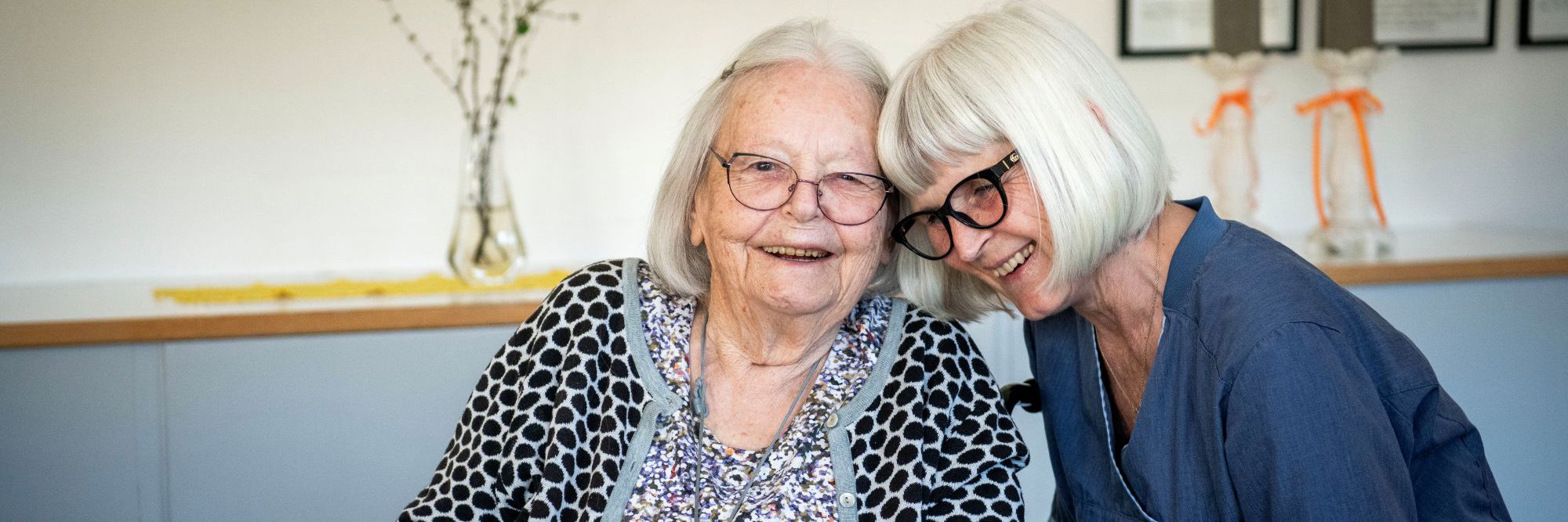 To damer, en borger og en plejepersonale, sidder med hovederne sammen og smiler