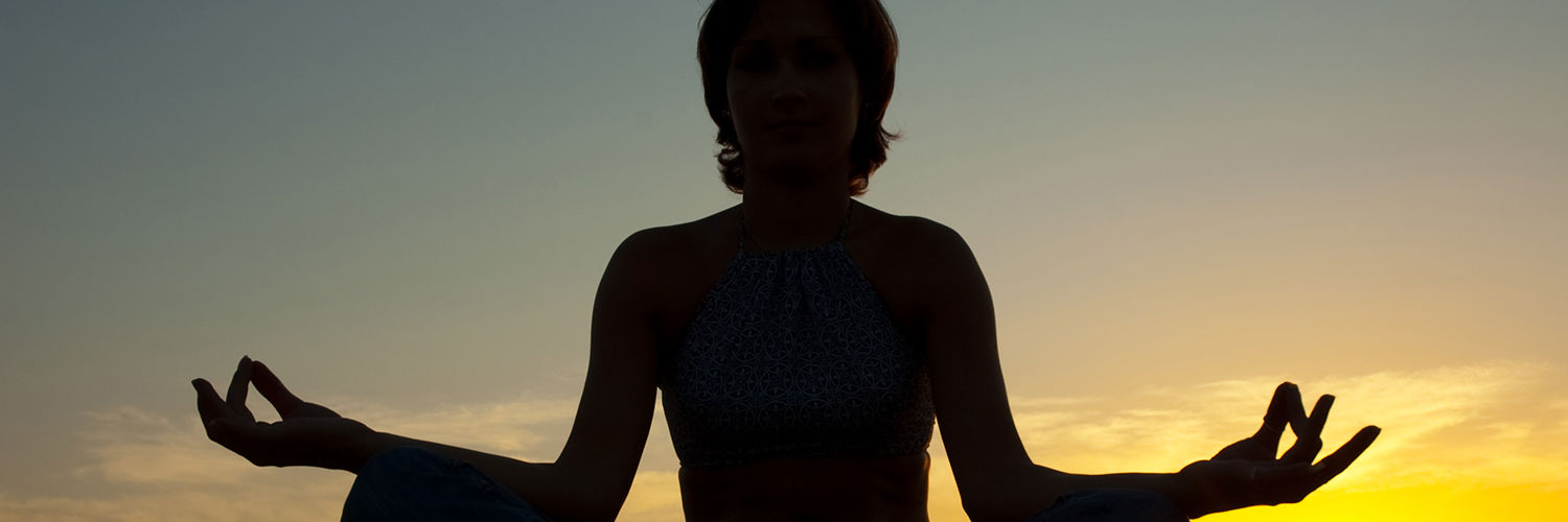 Dame der sidder og meditere ved solnedgang