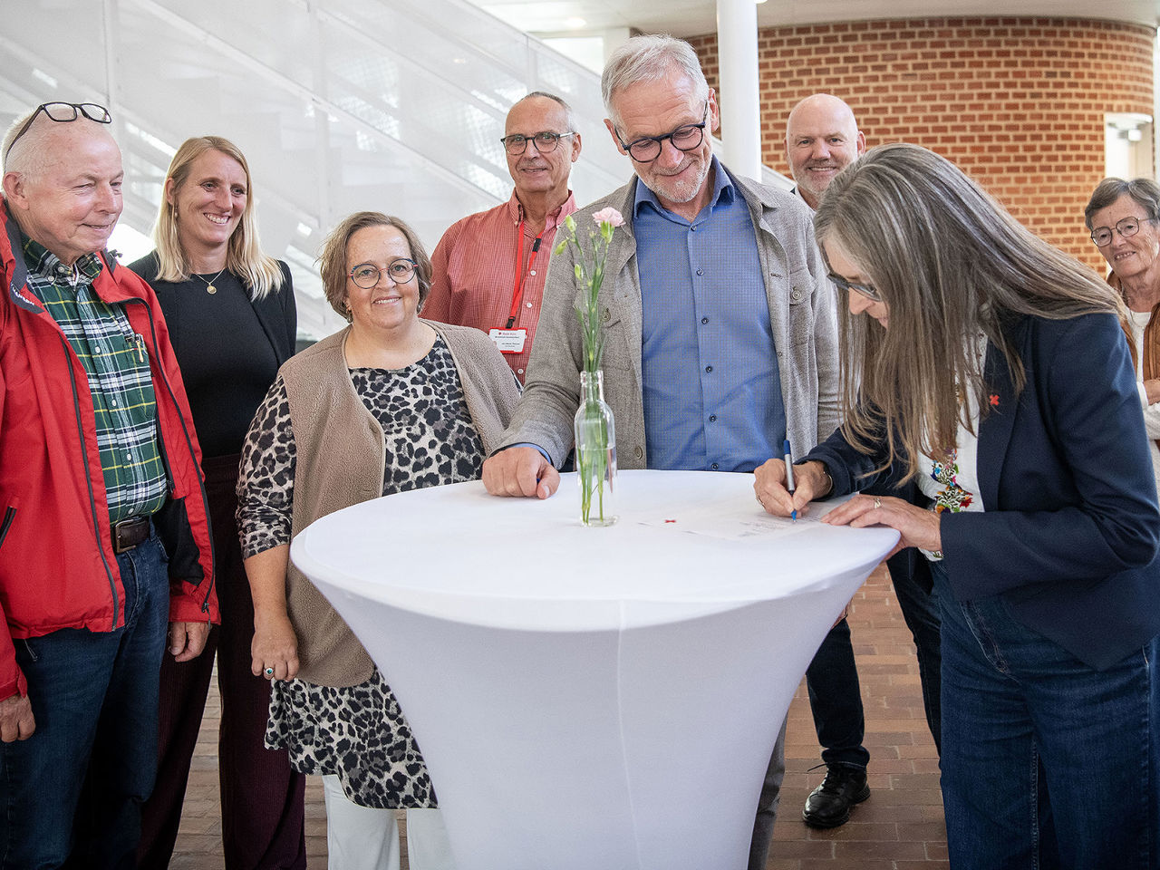 Otte personer rundt om et bord skriver under på et stykke papir.
