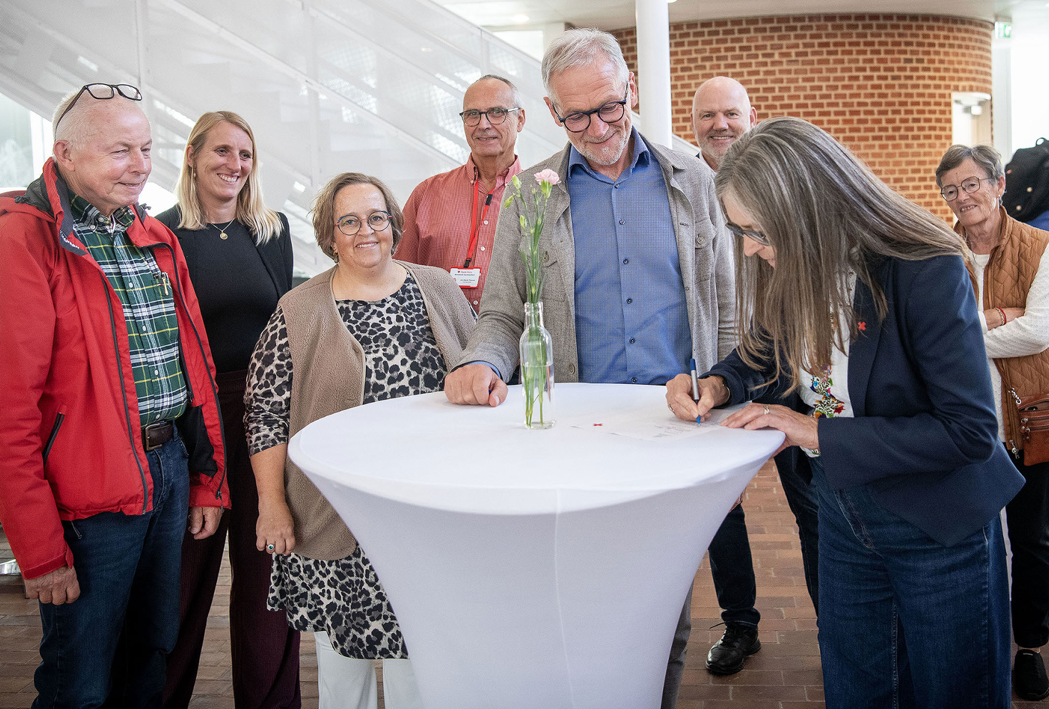 Otte personer rundt om et bord skriver under på et stykke papir.