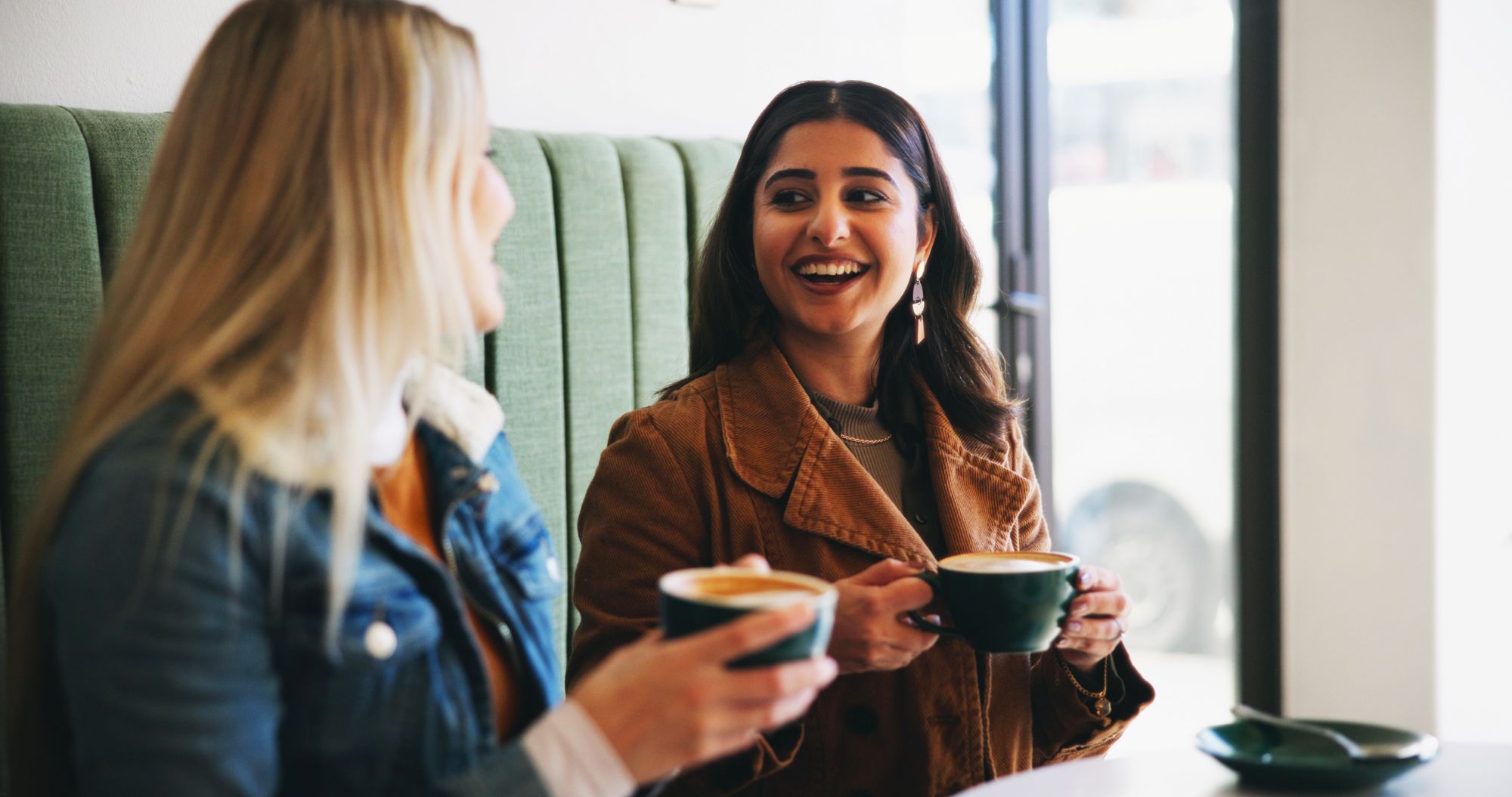 To unge kvinder drikker kaffe sammen og smiler