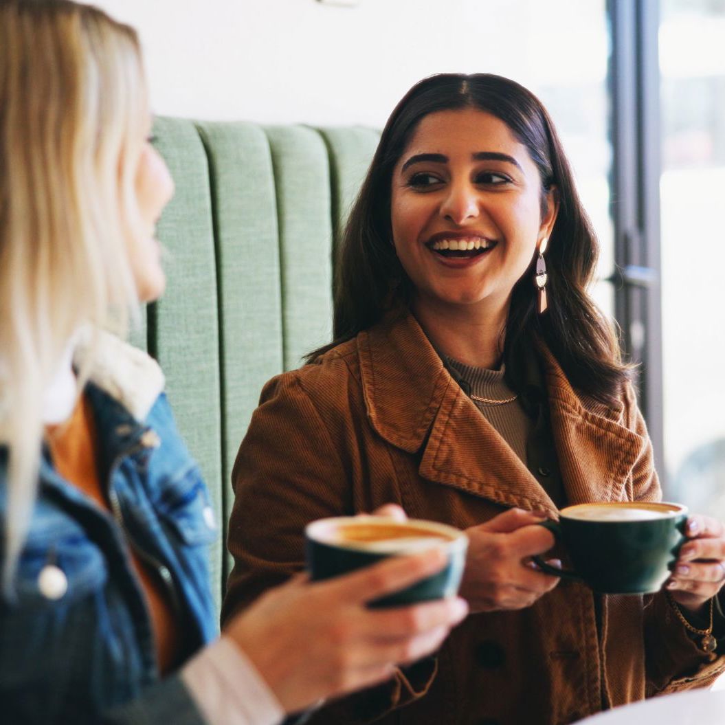 To unge kvinder drikker kaffe sammen og smiler