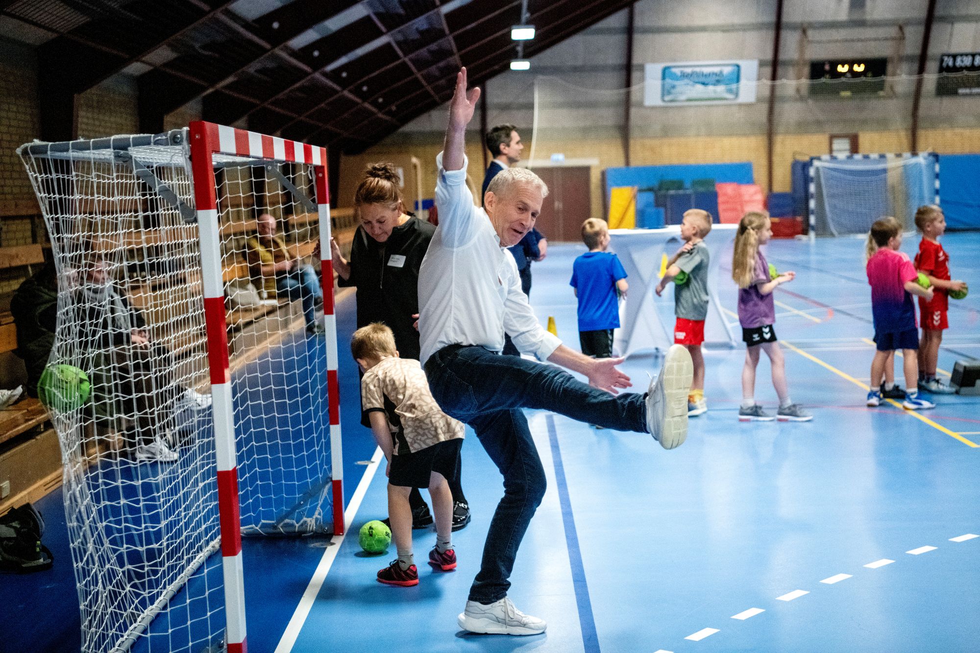 Skolebørn og voksne spiller håndbold i en hal