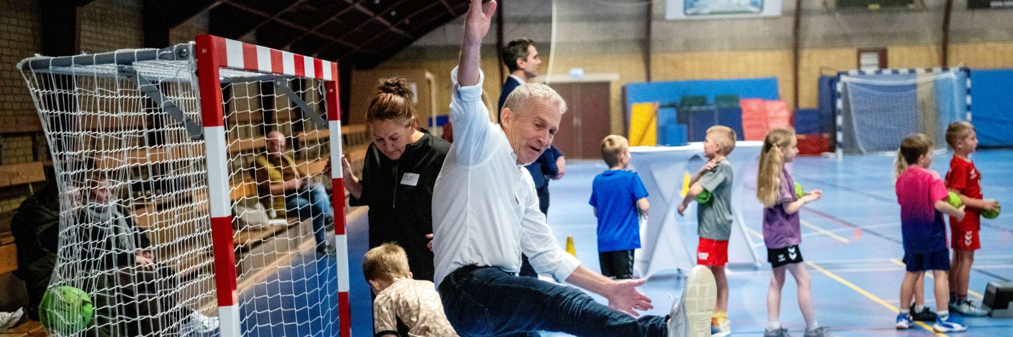 Skolebørn og voksne spiller håndbold i en hal
