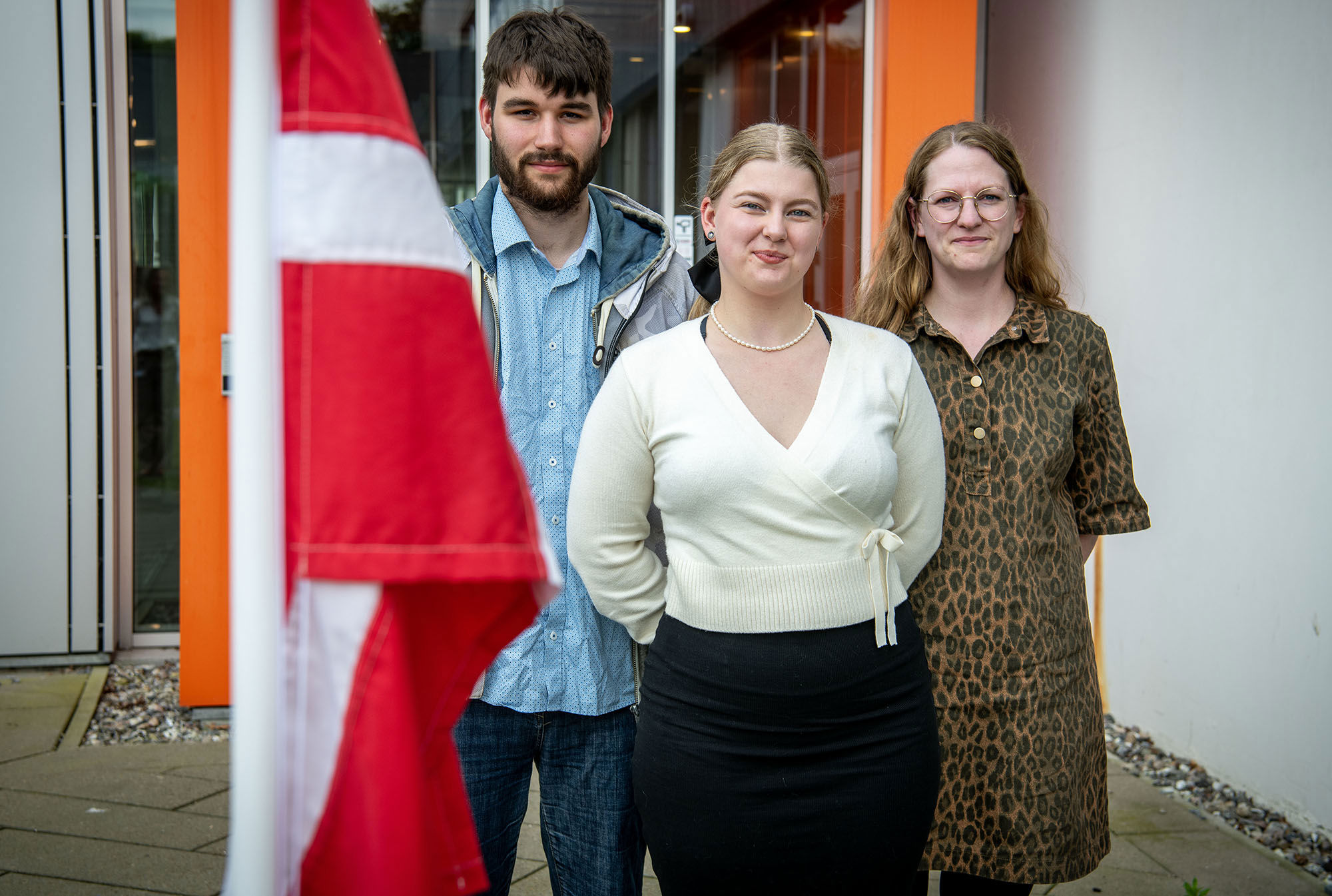 Tre unge personer med et Dannebrog i forgrunden