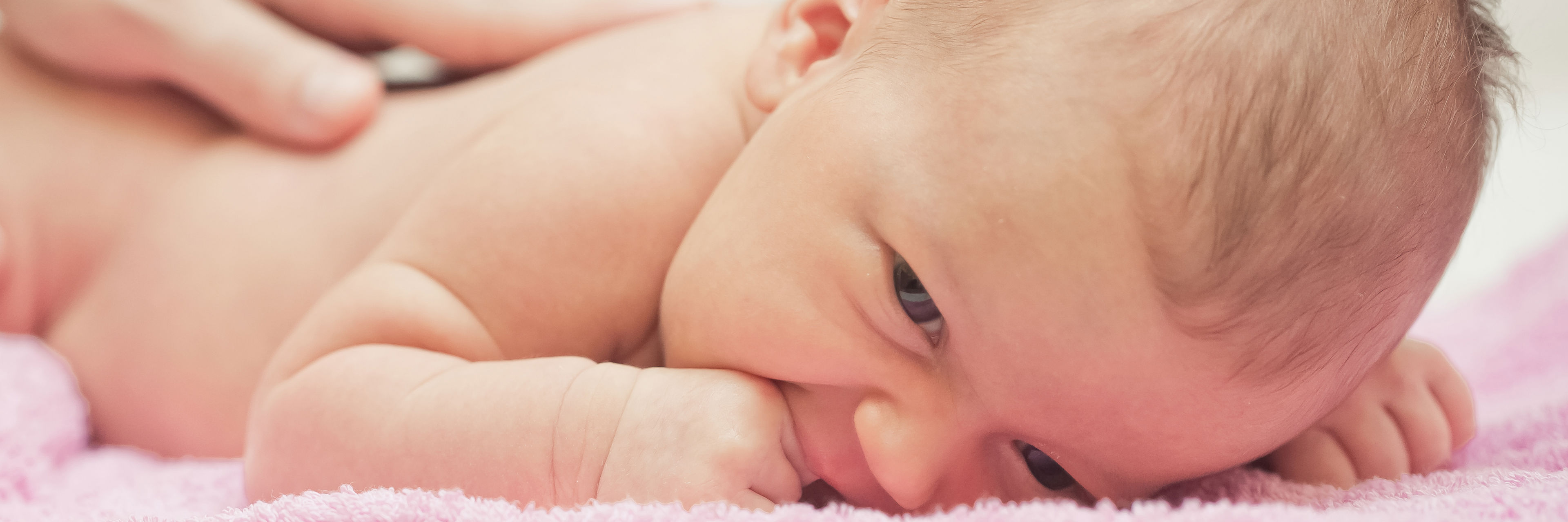 Baby der ligger på et lyserødt håndklæde og får massage